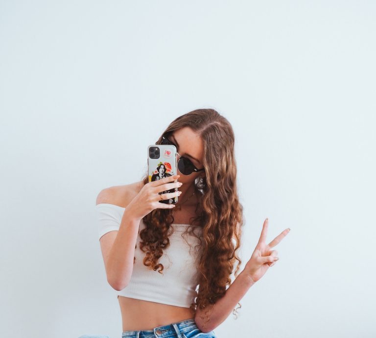 A woman holding a phone and giving the peace sign